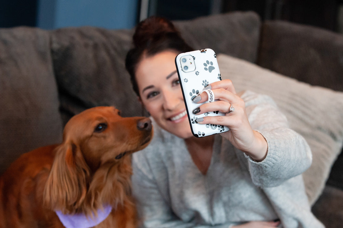 A woman taking a selfie with a dog while holding a Pawprints Loopy Case.