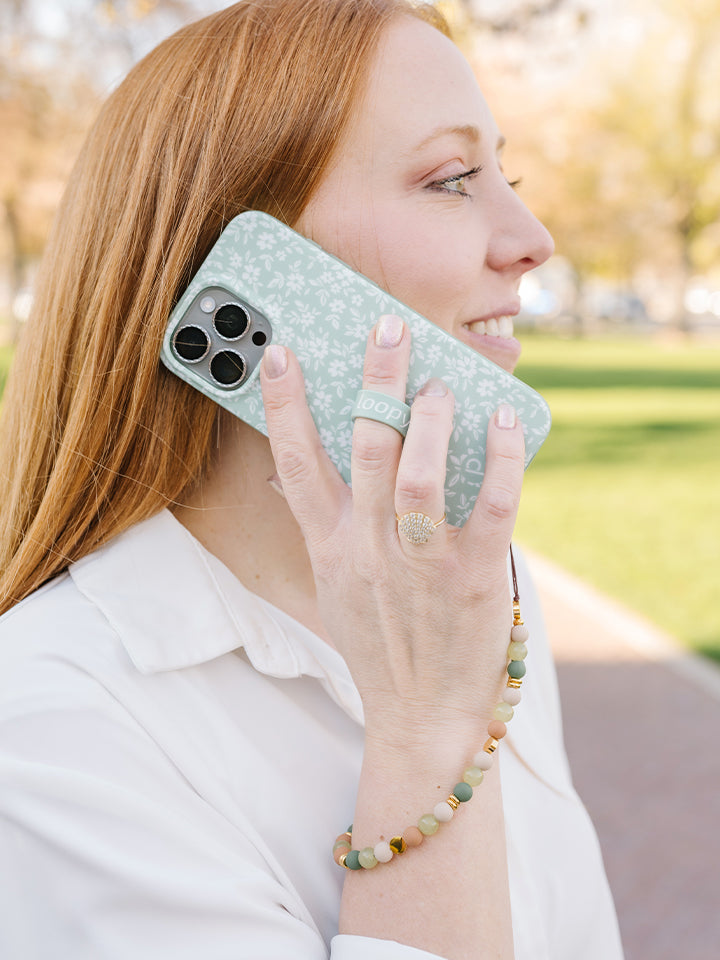 A woman wearing an Earthy Elegance Loopy Cases Wristlet that is attached to a Sage Floral Loopy Case.